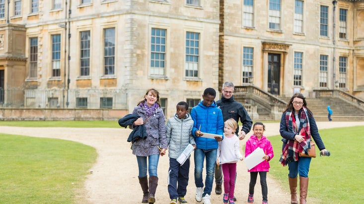 A family walking away from Belton House with trail sheets in hand.
